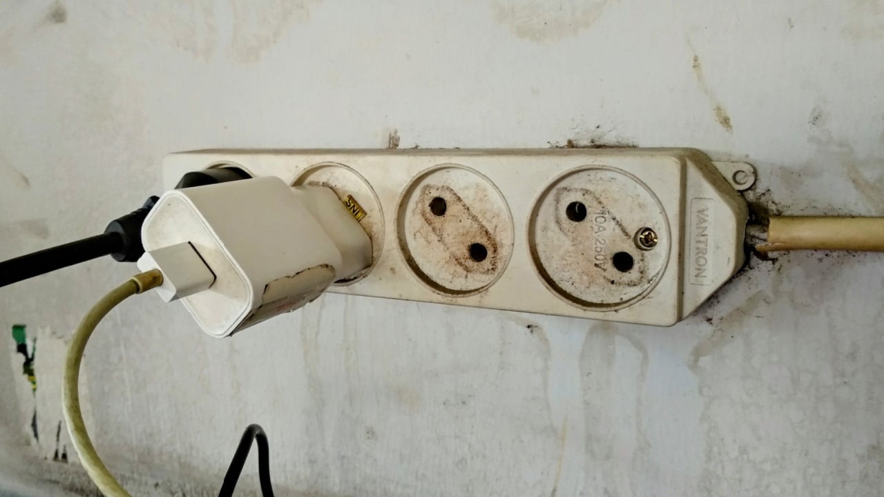 TULUNGAGUNG, INDONESIA - September 5, 2024: A simple yet telling image of a phone charger plugged into an old power strip.