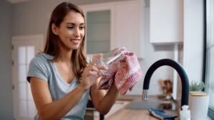 Young woman using cotton cloth while wiping glasses in the kitchen.