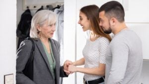 Young positive family couple meeting and joyfully greeting elderly woman at doorway