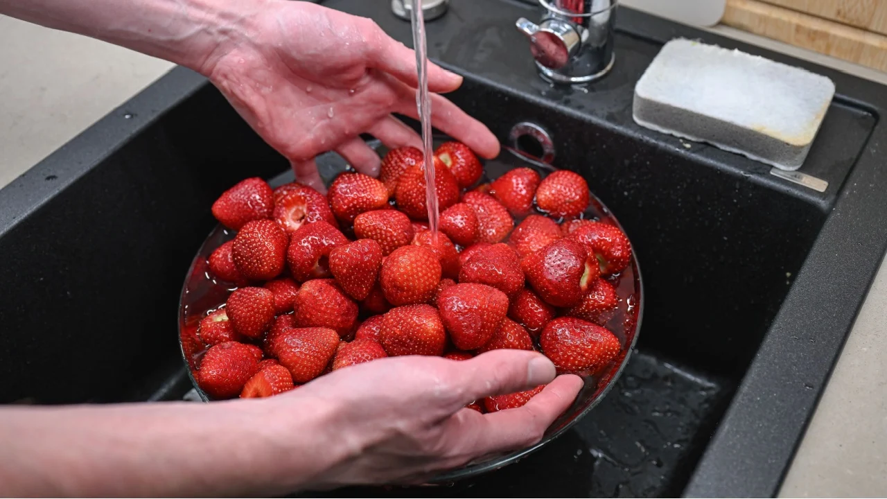 person washes fresh strawberries in the kitchen sink