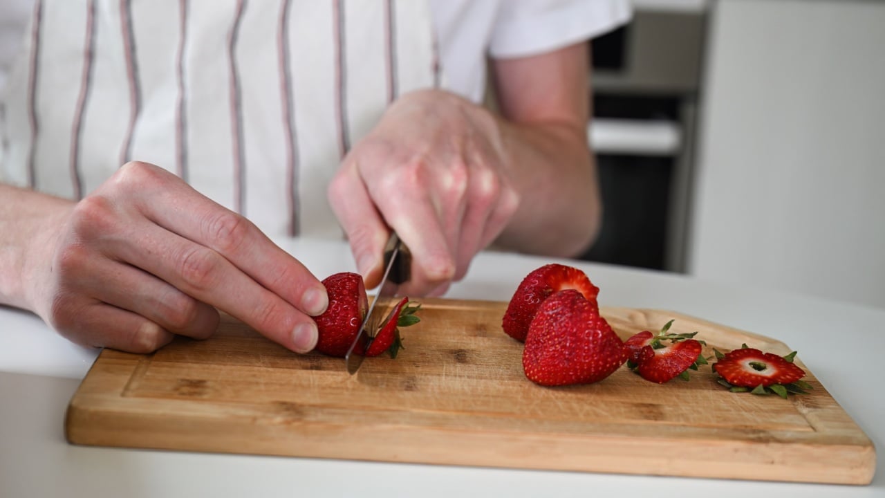 Person peels strawberries on the kitchen table, making sweet strawberry jam