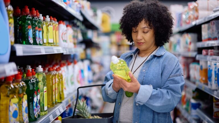Mature woman reading label on package while buying groceries at supermarket.