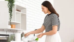 Beautiful young happy woman wiping plates with paper towels in kitchen