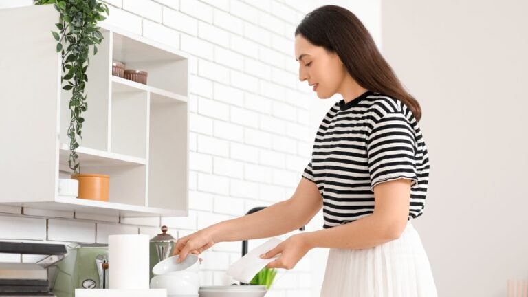 Beautiful young happy woman wiping plates with paper towels in kitchen