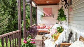 View of a modern-style summer veranda interior decorated with bright summer flowers, rattan rocking chairs, and a large pink sofa