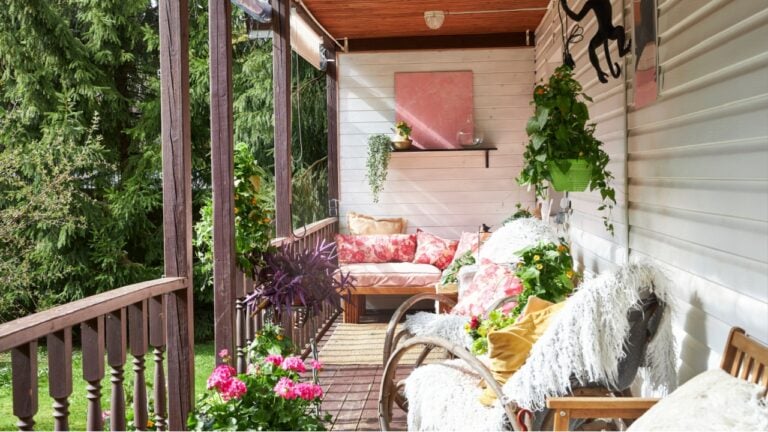 View of a modern-style summer veranda interior decorated with bright summer flowers, rattan rocking chairs, and a large pink sofa