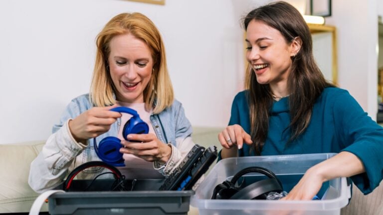 Two girls are holding a box with old computer parts, getting ready to recycle or donate them.