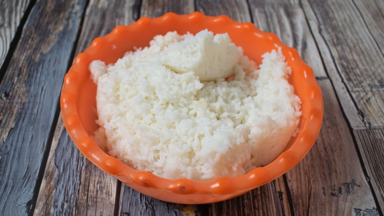 Steamed white rice served in a bright orange bowl on a rustic wooden table.