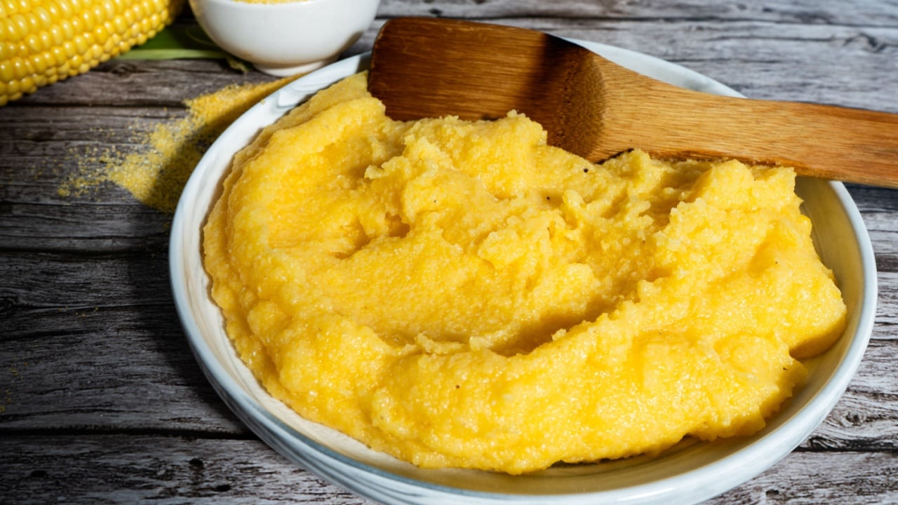 Delicious polenta is being served on a rustic wooden table, accompanied by fresh corn on the cob and cornmeal