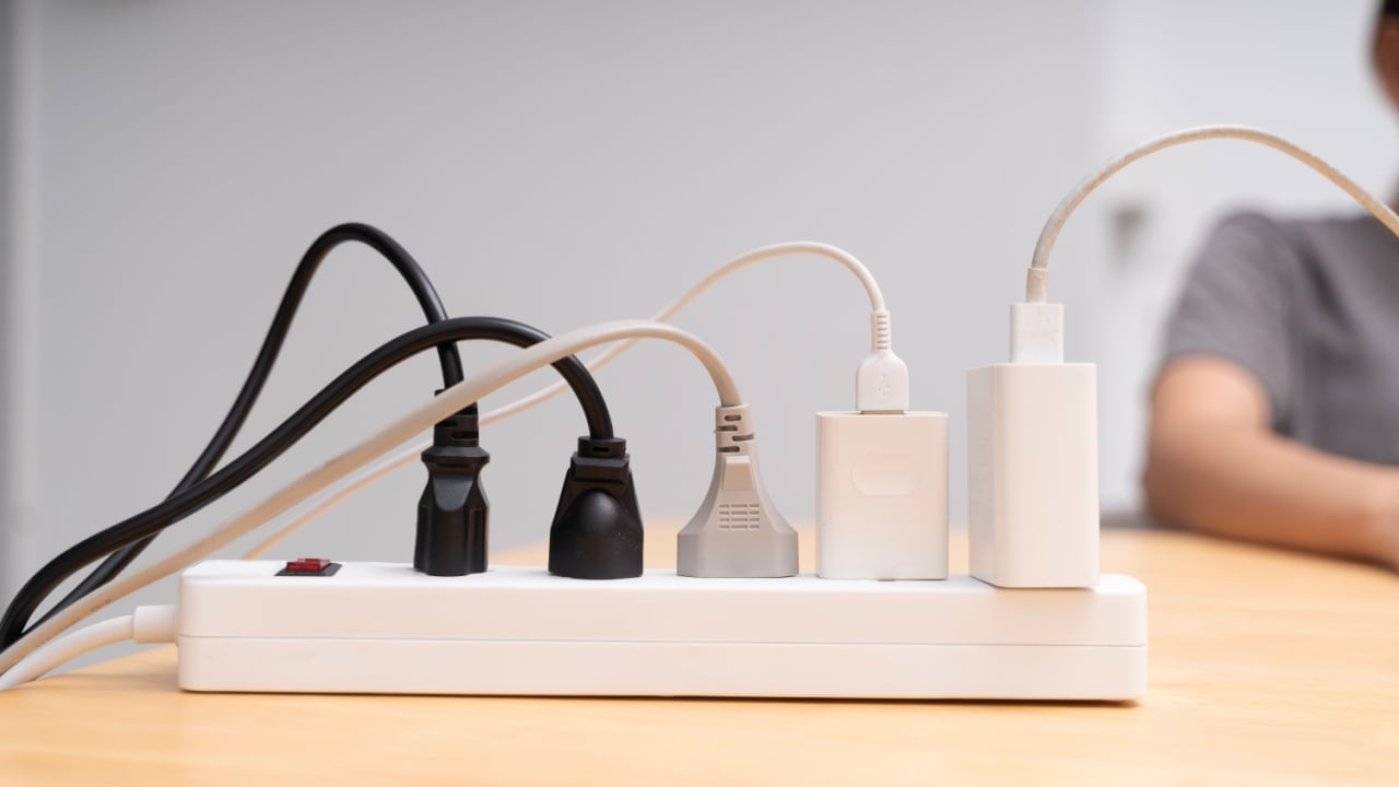 Close up of power strip with multiple plugs and tangled cables on wooden desk. Concept of electricity, energy supply, power connection, safety, and modern lifestyle with electronic devices at home.