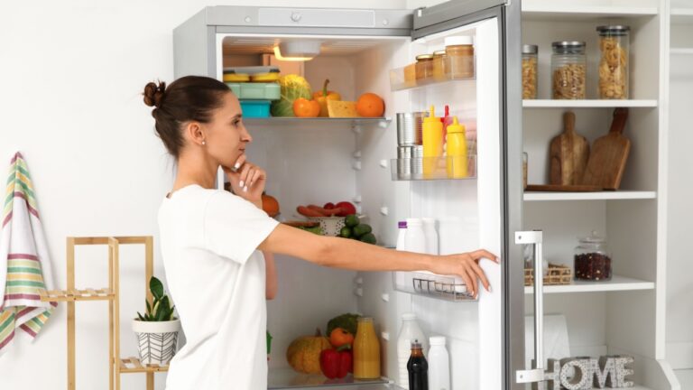 Thoughtful young woman near open fridge in kitchen