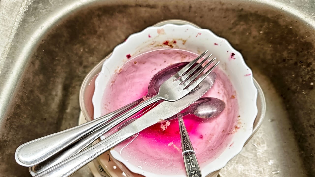Dirty dishes with pink water and utensils fill a kitchen sink, showing remnants of a recent home-cooked meal and the need for cleaning.