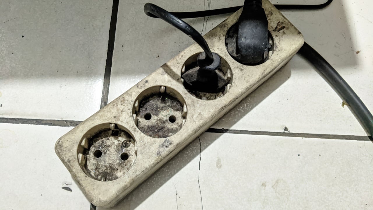 The electric extension cord shows signs of heavy use, dust, and stains, with two plugs connected and two unused sockets visibly corroded.