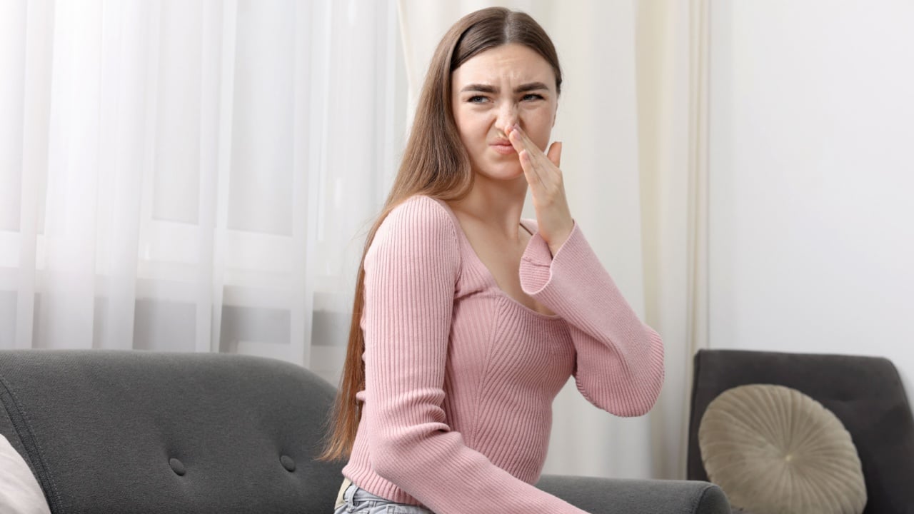 Young woman suffering from bad smell and covering her nose indoors