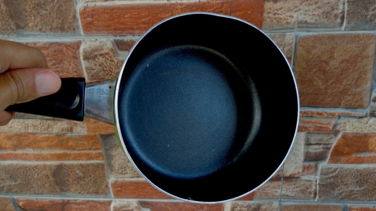 A hand holding a small nonstick pan against a brick wall background.