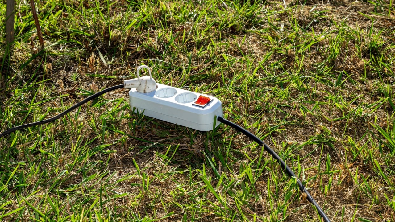 A white power strip placed on vibrant green grass represents the blend of technology and nature for outdoor activities, selective focus