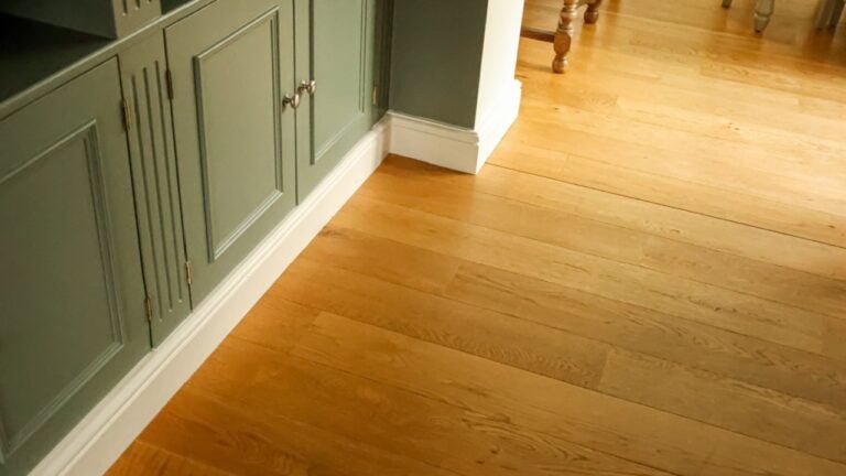Home interior details showing light hardwood flooring planks meeting a painted cabinet with paneling and white baseboards