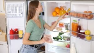 Woman with ham near open refrigerator in kitchen