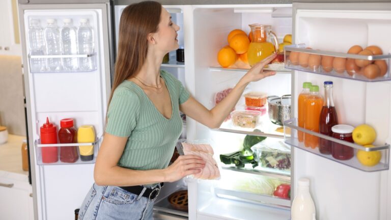 Woman with ham near open refrigerator in kitchen
