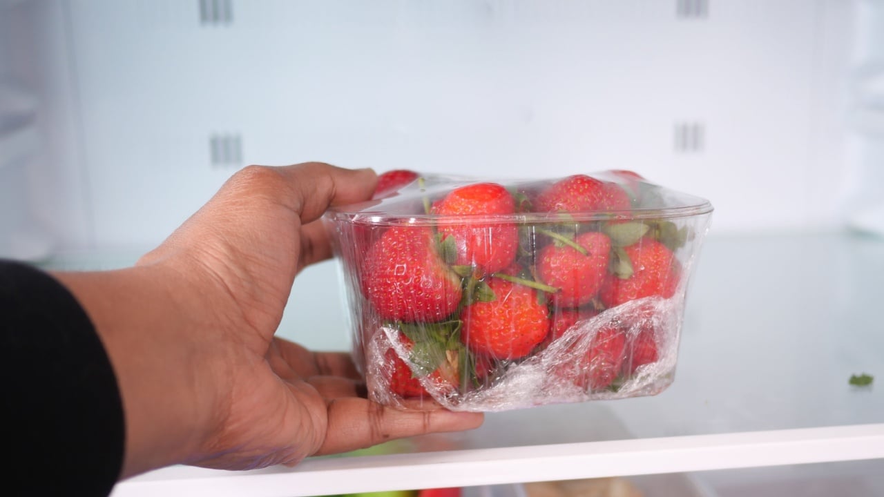 Hand holding a container of strawberries in a fridge