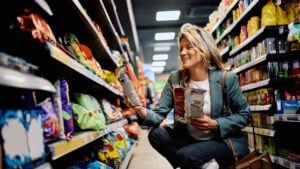 Happy woman taking snacks from a shelf while buying groceries in supermarket.