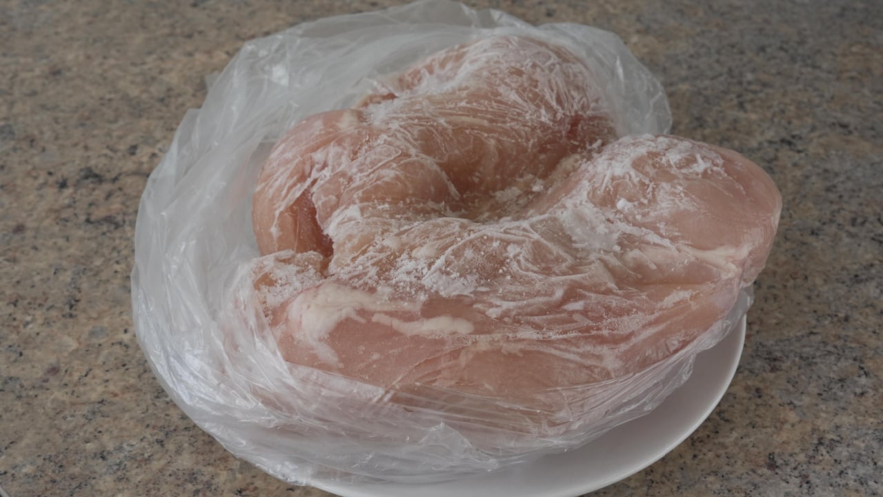 Frozen Raw Chicken Breast in Plastic Bag on Plate