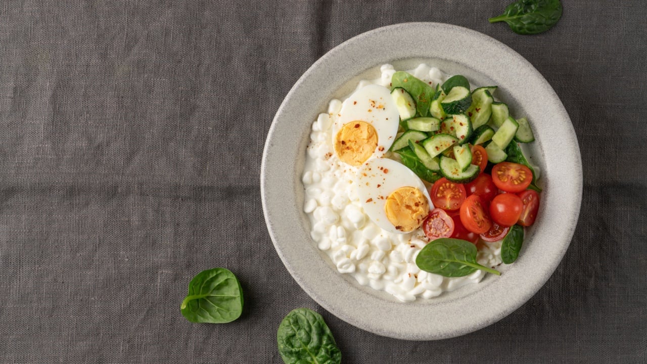 Fresh high protein savory cottage cheese bowl with cherry tomatoes, cucumber, boiled egg and chili flakes served on dark gray linen fabric background with copy space. Modern wellness and clean eating concept, balanced protein-rich meal, gut health friendly and aesthetic healthy lifestyle lunch or snack