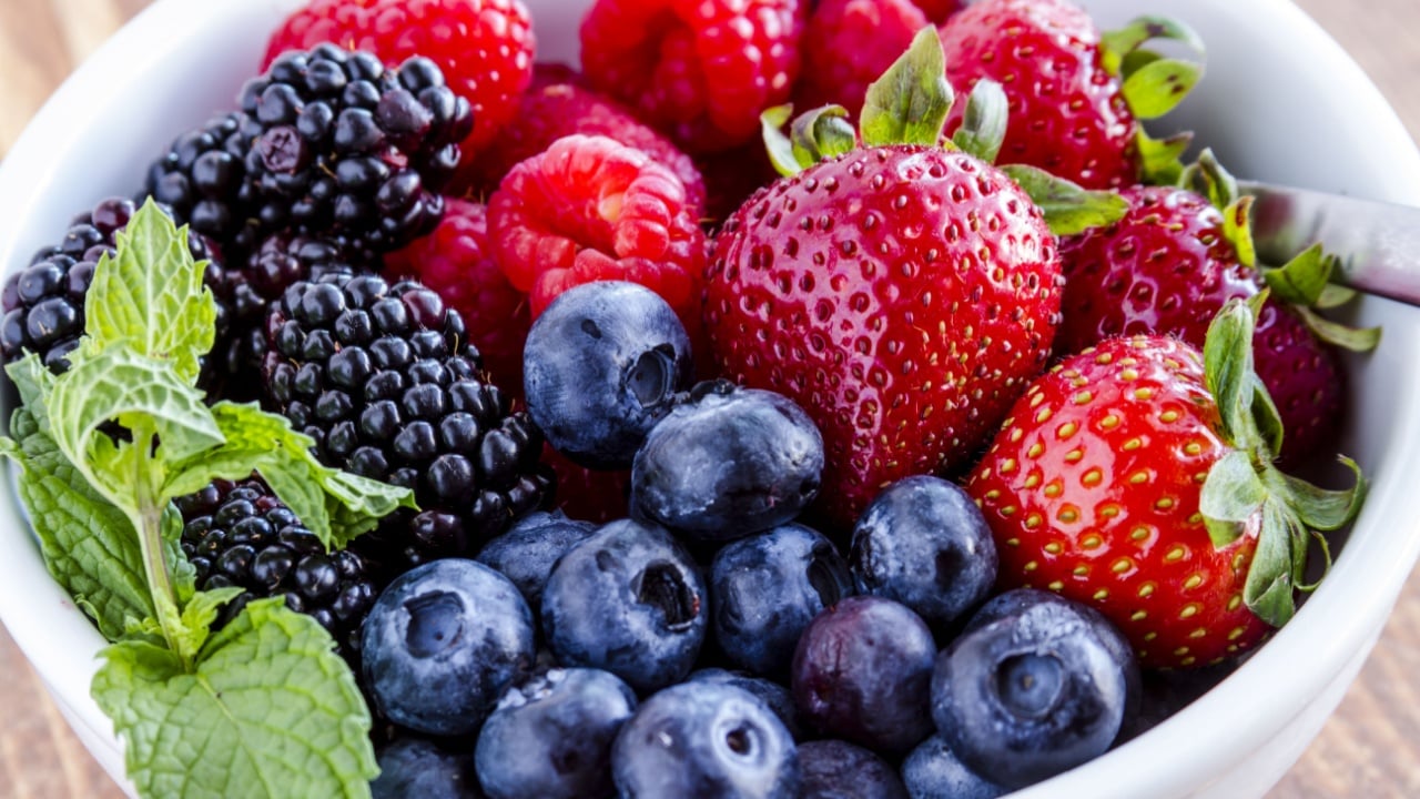 Close up of white bowl filled with fresh organic blueberries, blackberries, raspberries and strawberries garnished with mint leaves