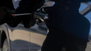 Criminal in black clothes attempting to break into a parked car at night, concept of car theft, security risk, and crime prevention.