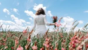 Back view of woman in long white dress with a wildflower bouquet in pink flower field