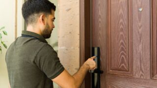 Hispanic man in front of a smart lock on a door, using a digital touchscreen keypad to enter his house