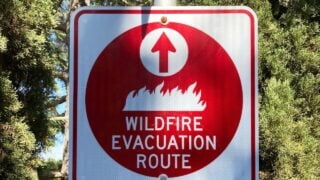 Red wildfire evacuation route sign with ahead arrow that point in the correct direction of voluntary or mandatory egress during fire emergency.