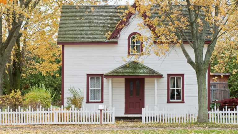 A red and white house sits on a treelined street