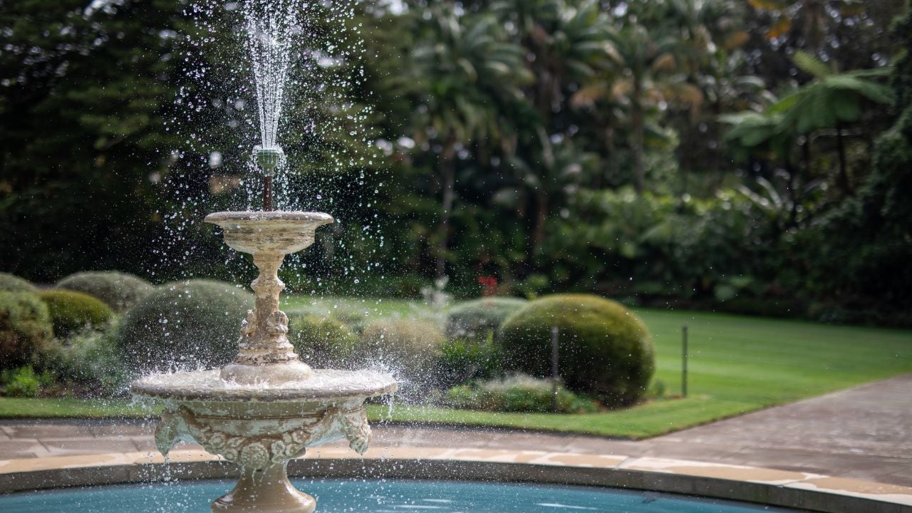 A classic stone fountain sprays water in a tranquil garden setting.