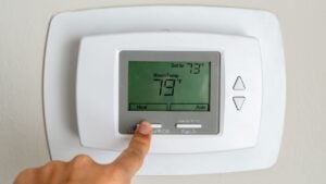 A finger switching the mode on the white thermostat to heating, adjusting the function to warm up the apartment for added comfort during colder weather