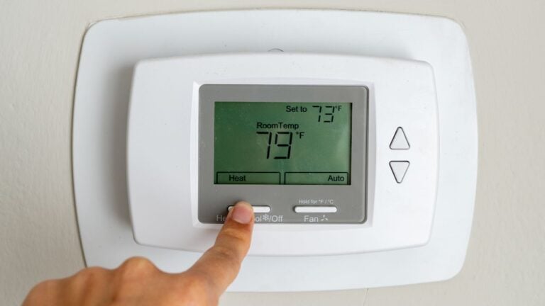 A finger switching the mode on the white thermostat to heating, adjusting the function to warm up the apartment for added comfort during colder weather
