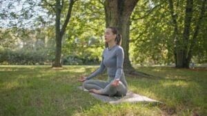 A young beautiful white girl practices yoga in the park and meditates in the lotus position among the trees in a clearing on a summer day. High quality image