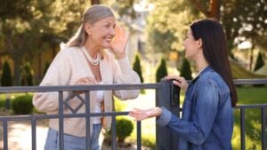 Friendly relationship with neighbours. Happy women talking near fence outdoors