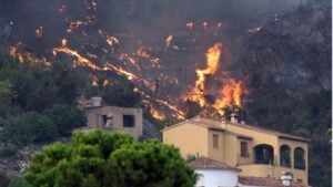 Intense wildfire engulfs homes and trees on a steep mountain slope with flying embers
