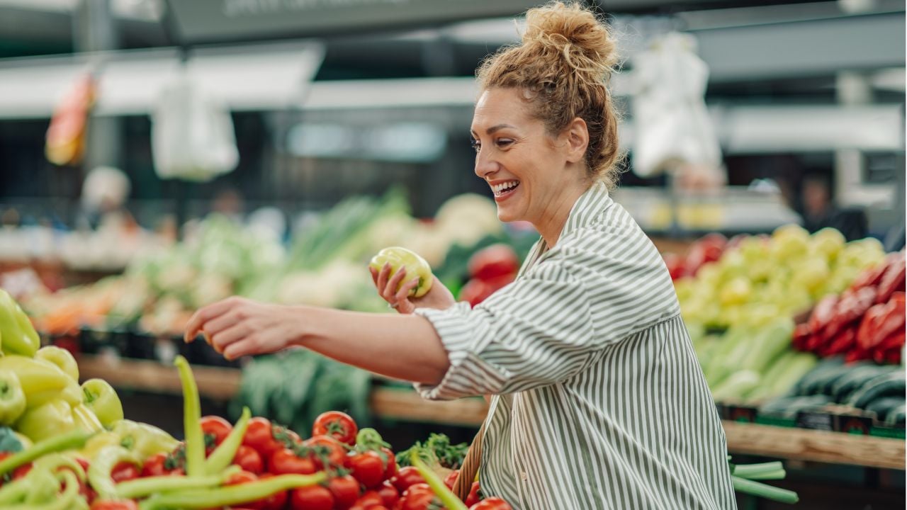 Portrait of a happy customer choosing and buying fresh organic vegetables at food market. Smiling shopper woman picking fresh vegetables from market stall at farmers market.