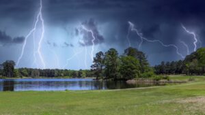 a gorgeous summer landscape with a rippling blue lake with lush green trees reflecting off the water with powerful storm clouds and lightning at Callaway Gardens.