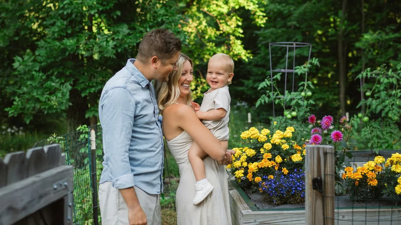 A man and woman holding a baby in a garden.