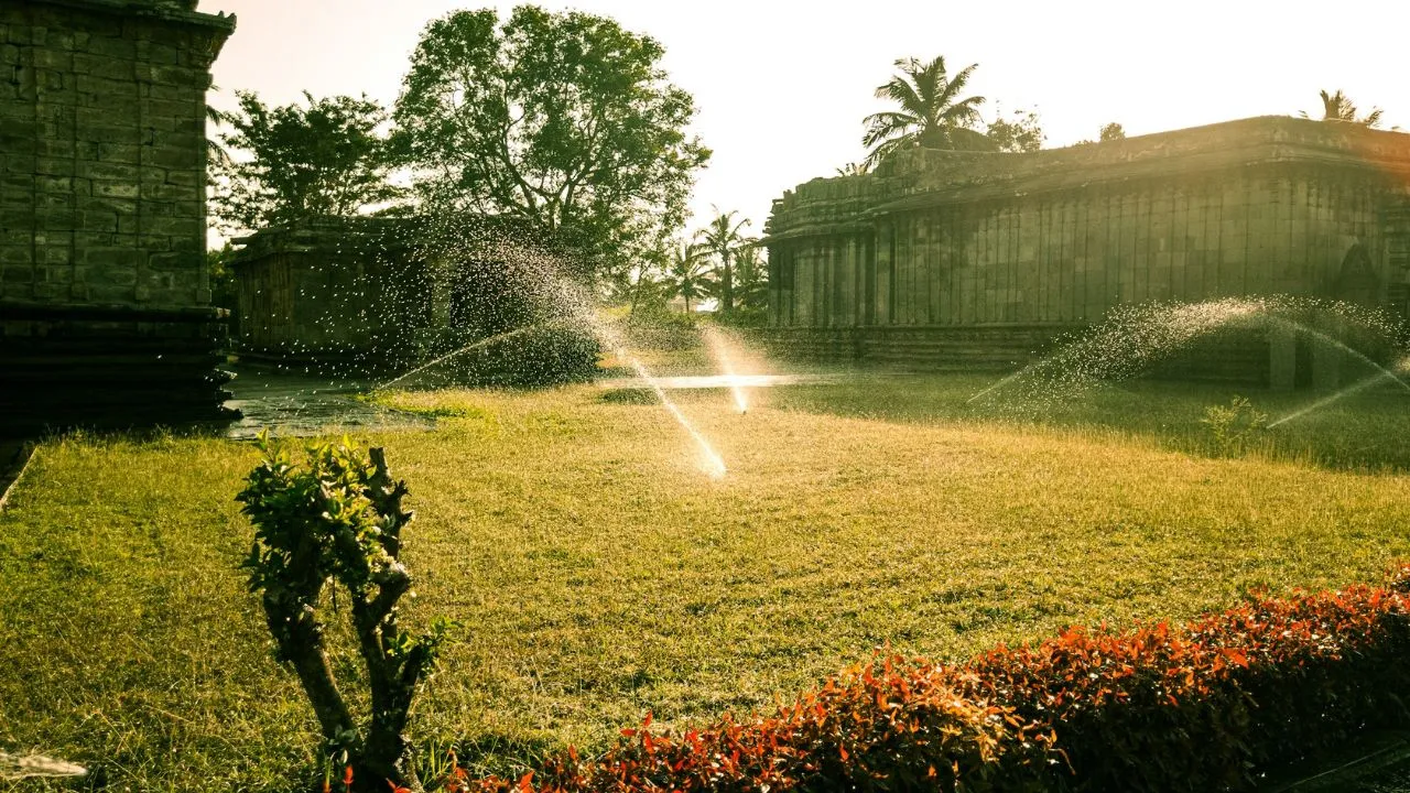 Sprinklers watering a grassy area near old buildings.