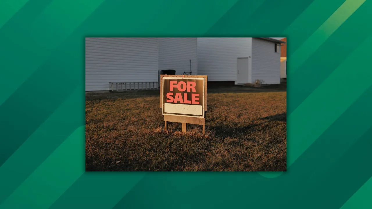 Close-up of a 'For Sale' sign in a suburban yard, indicating a property for sale.